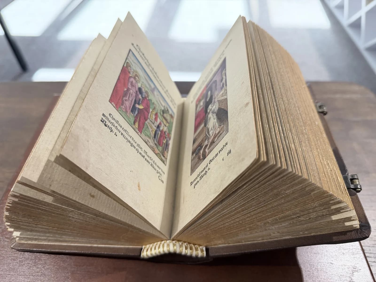 Niewielka otwarta księga z ręcznie kolorowanymi rycinami scen biblijnych.
